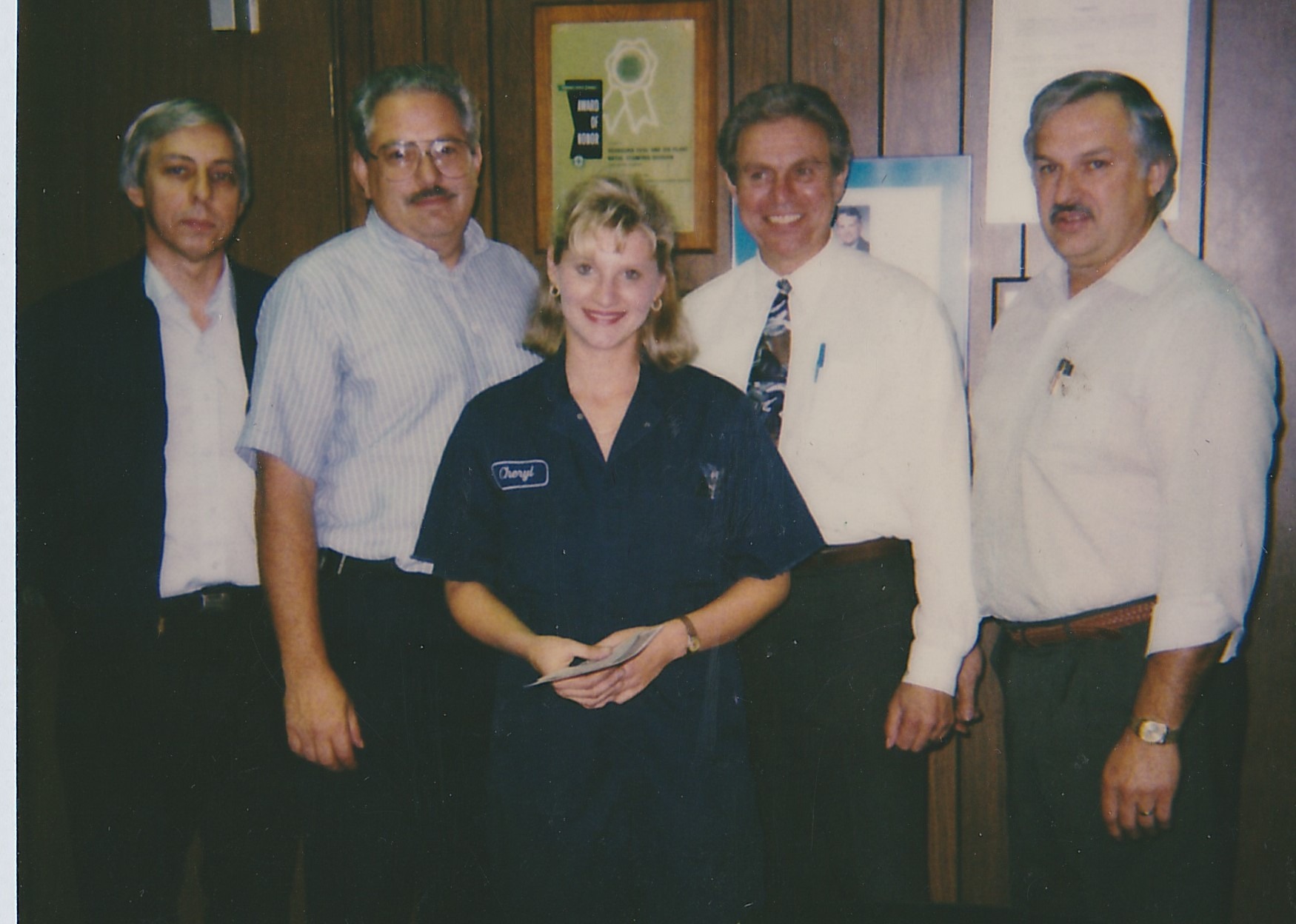 A young Cheryl Thompson in a navy Ford work shirt with her name patch, holding a certificate, standing with four managers.